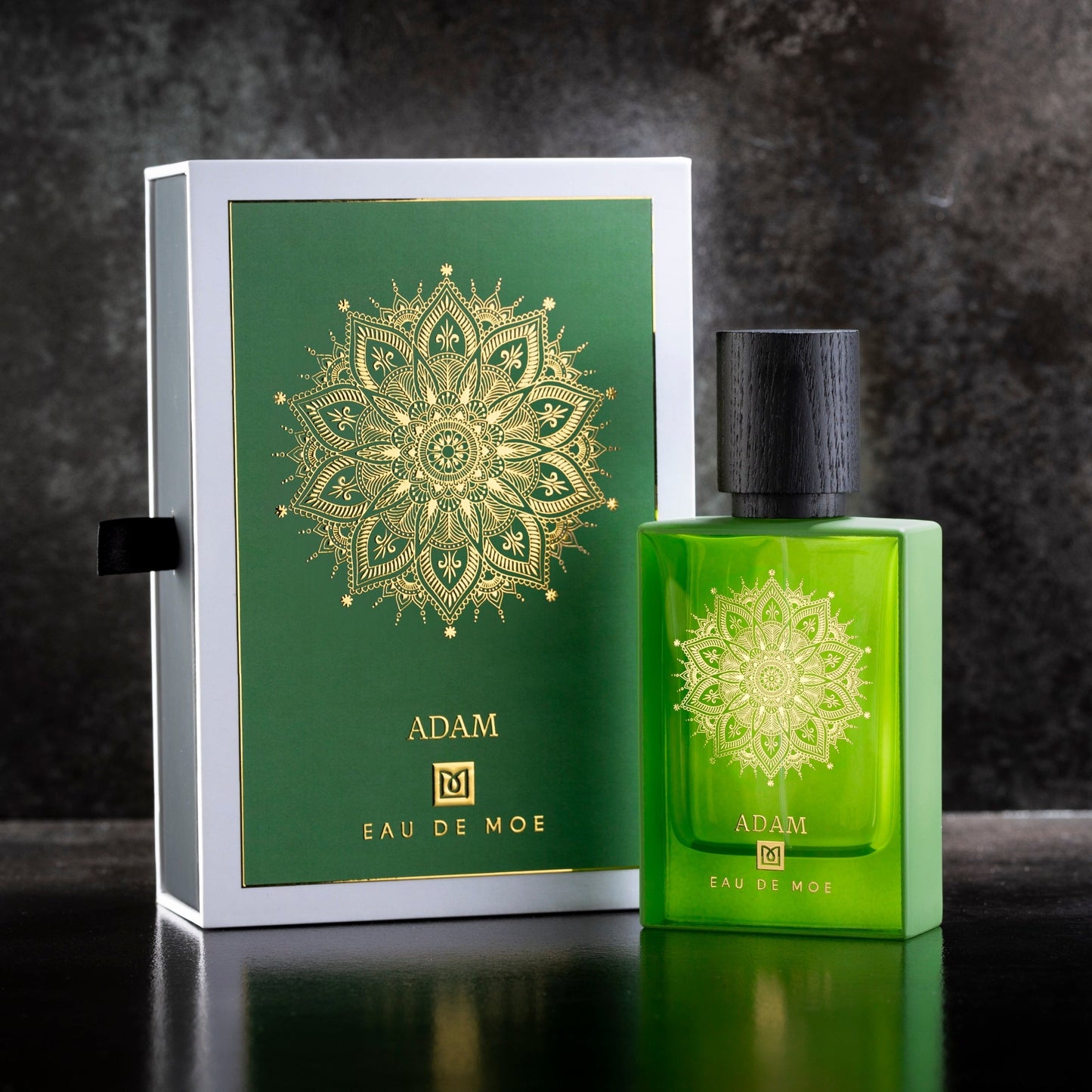 A green ADAM Eau de Parfum bottle by Eau De Moe stands beside a matching green and gold mandala-patterned box. This men’s fragrance features Italian bergamot notes and is showcased on a dark surface.