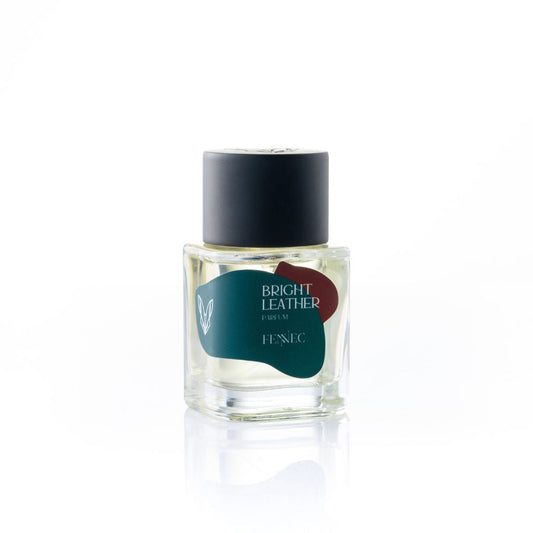 A clear glass perfume bottle labeled Bright Leather Parfum by Fennec, featuring a black cap and green-red abstract logo, inspired by vibrant North African tropical fruit scents, is set against a plain white background.