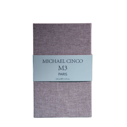 A rectangular box with a textured lavender surface and a light gray label reading Fragrapedia Haus M3 Eau de Parfum 100 ml, suggesting a floral scent created by Michael Cinco with consciously sourced ingredients.