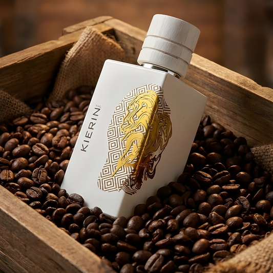 A bottle of Cafe Kiss Eau de Parfum by Fragrapedia Haus, featuring gold and brown art, rests on coffee beans in a wooden crate, evoking the cozy allure and rich coffee notes of this unique fragrance.