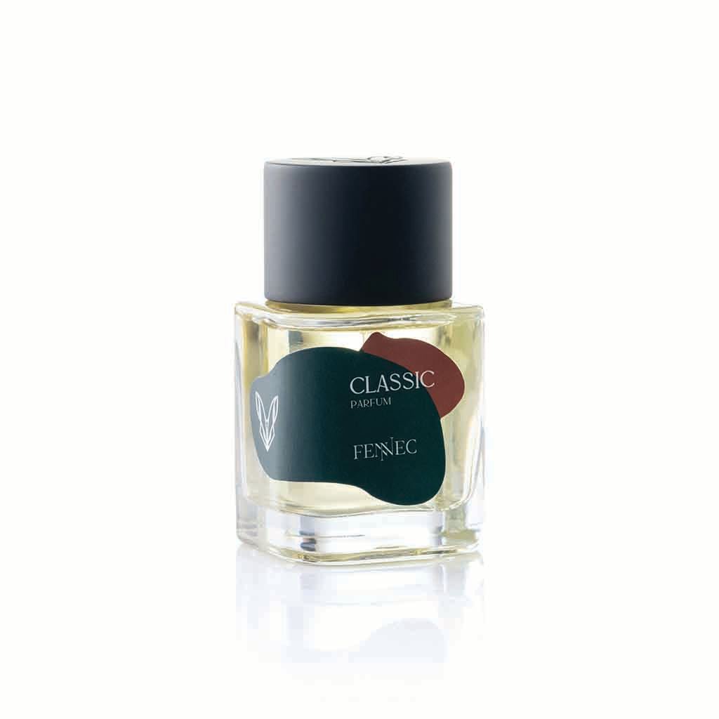 A clear glass bottle of Classic Parfum by Fennec, with a black cap and a label featuring a green and red abstract design inspired by the North African desert fox, is shown against a white background.