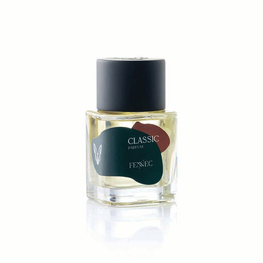 A clear glass bottle of Classic Parfum by Fennec, with a black cap and a label featuring a green and red abstract design inspired by the North African desert fox, is shown against a white background.