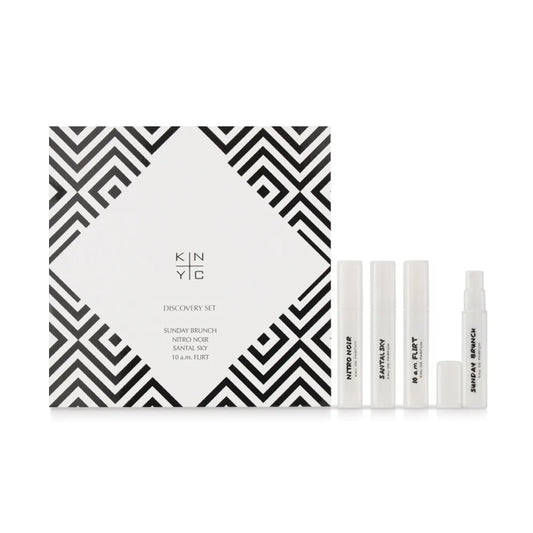A black and white Kierin Discovery Set box labeled KINYC is shown with four white spray bottles in front, each a sample of Kierin Premium Eau de Parfums: NITRO NOIR, SANTAL SKY, 10 a.m. FLIRT, and SUNDAY BRUNCH.