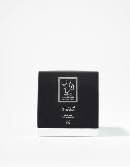 A black and white box labeled "Ahojas Oud Mubakhar - Hind Al Oud" by Hind Al Oud stands upright against a plain white background, evoking the rich allure of oud perfume.