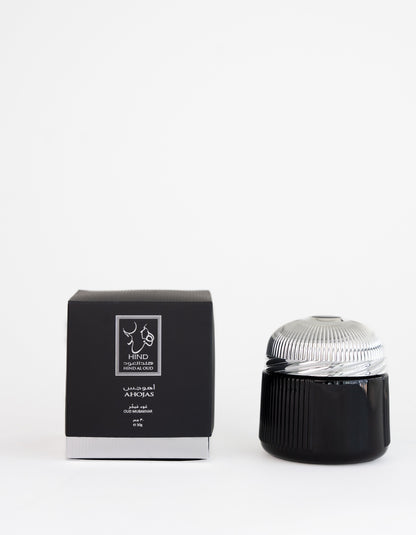 A black and silver Ahojas Oud Mubakhar jar by Hind Al Oud is displayed next to a matching black box with white text and the fragrance logo, set against a plain white background.