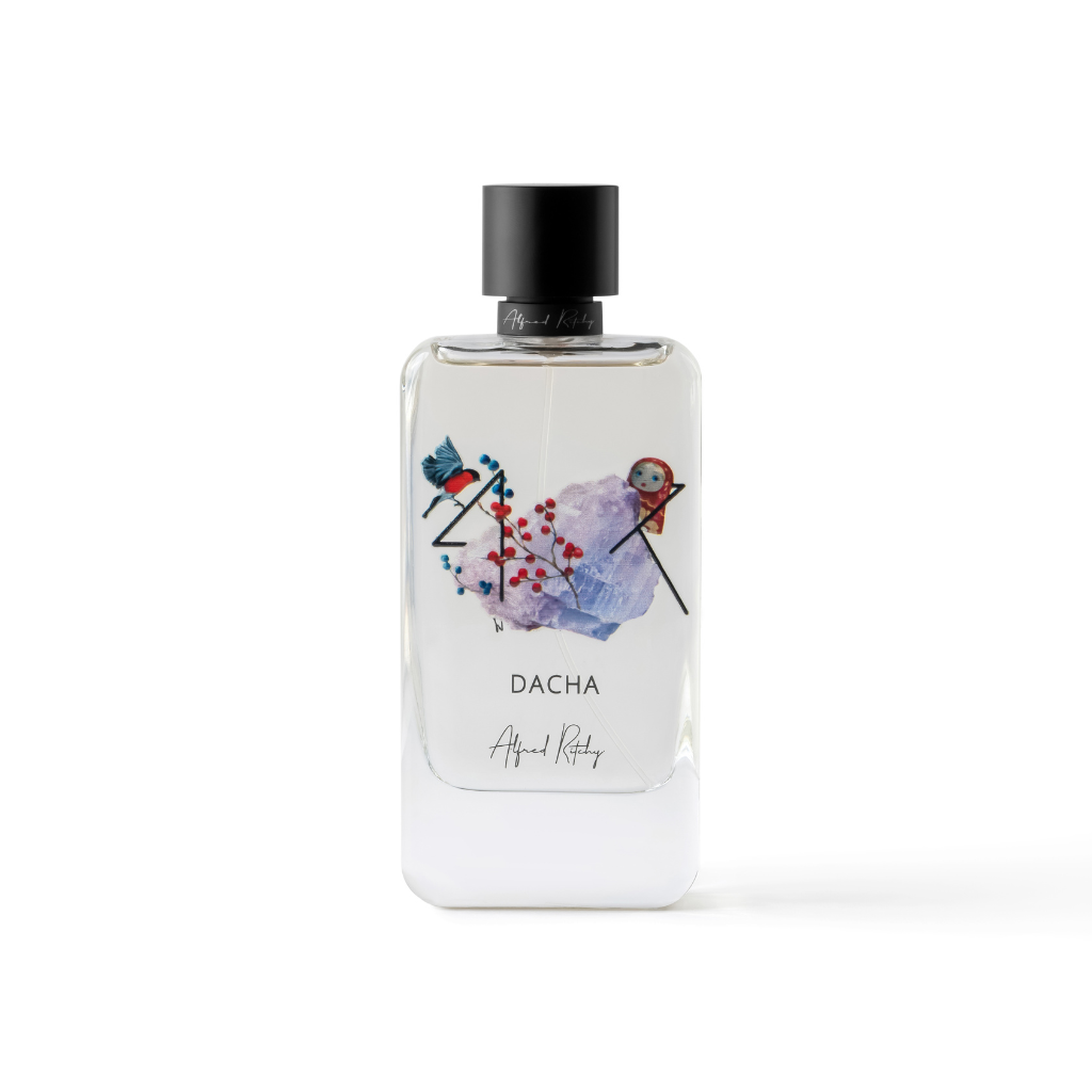 A clear 100ml DACHA Eau de Parfum bottle by Alfred Ritchy, featuring colorful abstract bird and berry art on the front, a sleek black cylindrical cap, and “Alfred Ritchy” at the base.