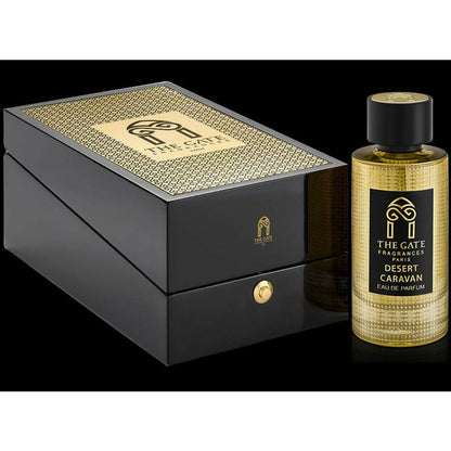 A bottle of Desert Caravan Eau de Parfum by The Gate Paris, an oriental spicy scent with oud musk notes, stands beside an elegant black and gold box showcasing the brand logo and geometric pattern against a black background.