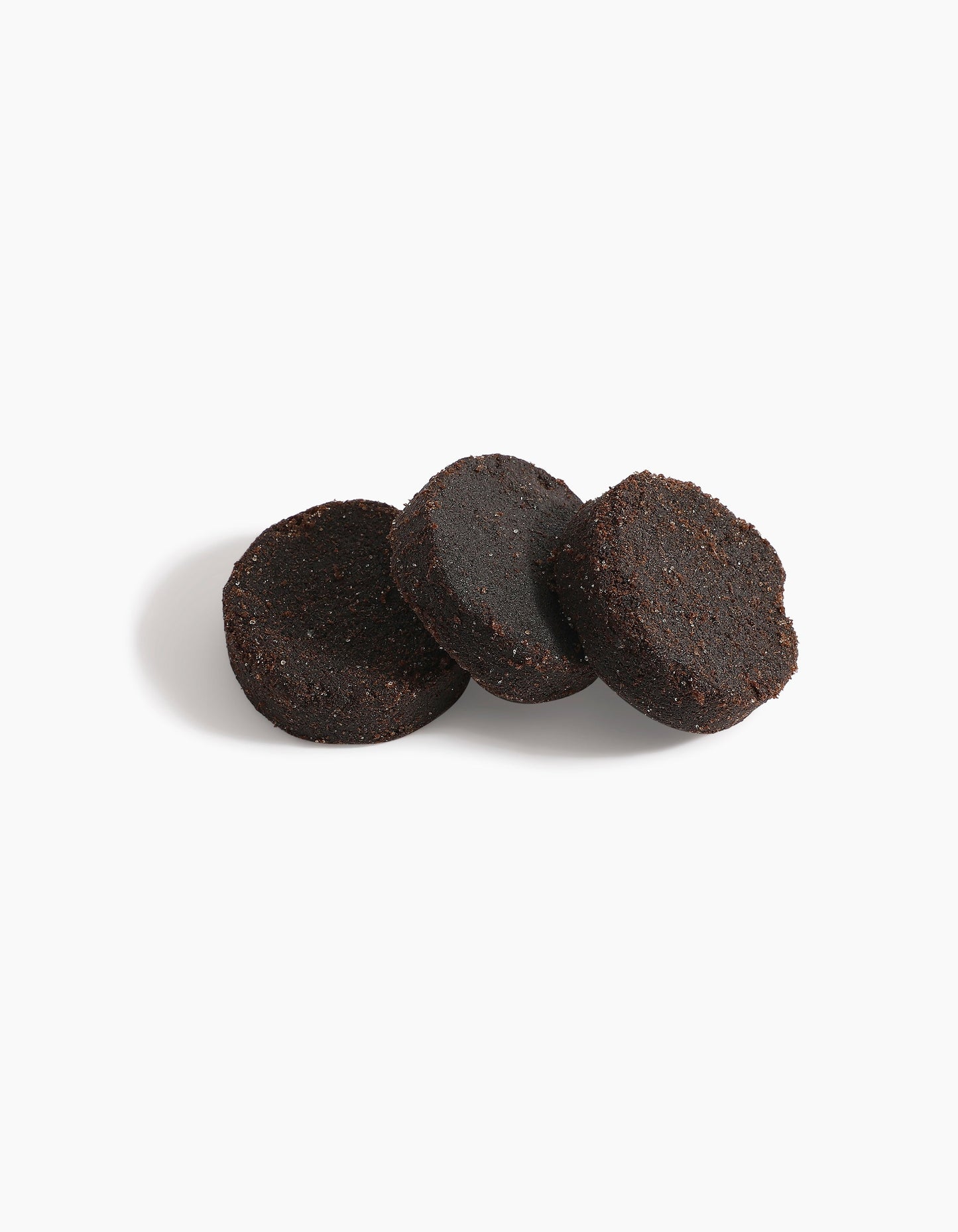 Three dark brown, round discs of used coffee grounds—evoking the rich tones of Al Shioukh Dokhoon by Hind Al Oud—are lined up on a white background with soft shadows to the left.