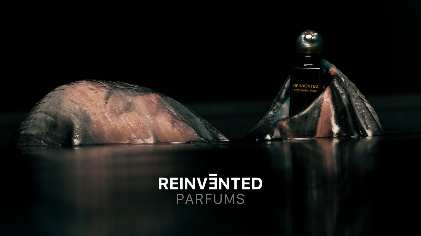 A hand emerges from dark water, holding the ENIGMATIC AURA Extrait de Parfum - Reinvented bottle by REINVĒNTED, with the brand bold at the bottom center—an image evoking luxury and vegan elegance.