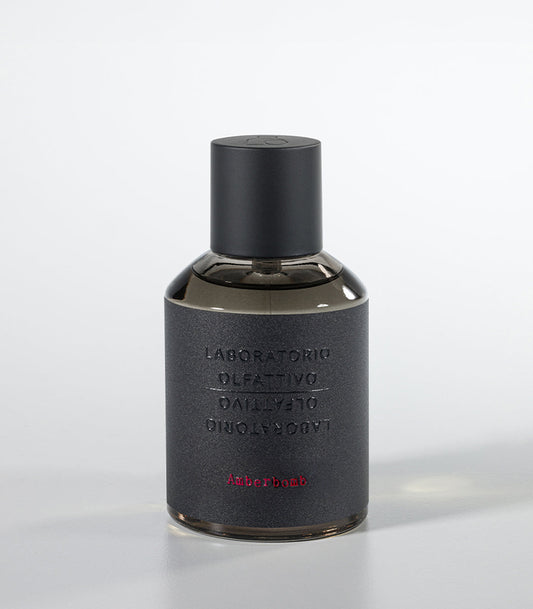 A dark, cylindrical Amberbomb Eau de Parfum bottle by Laboratorio Olfattivo features a matte black cap and textured gray label with silver brand text and red "Amberbomb," embodying the refined luxury of the Extreme Collection.