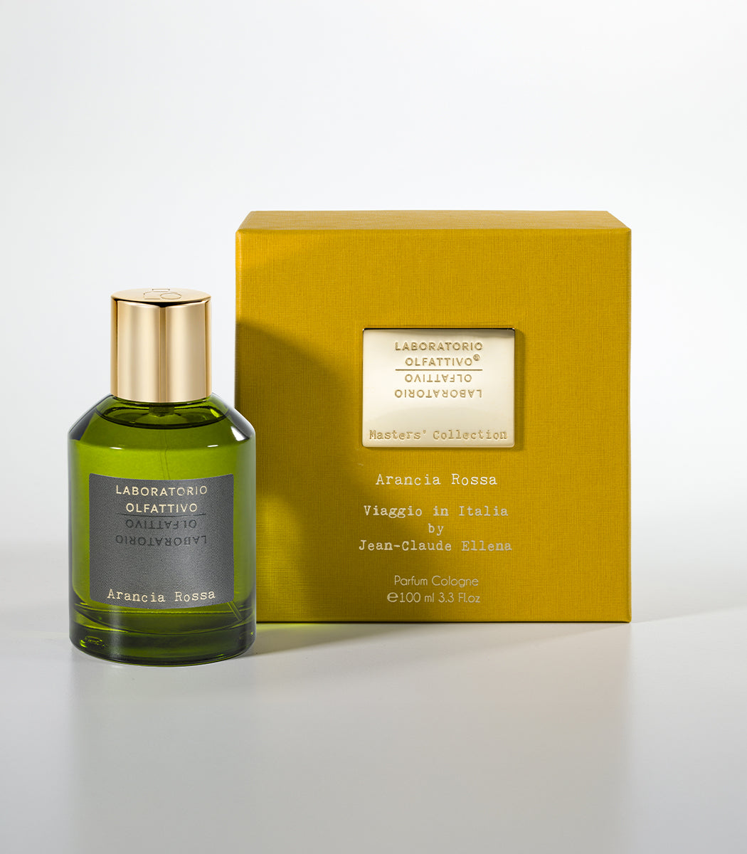 A green glass bottle with a gold cap, labeled “Arancia Rossa Eau de Parfum - Laboratorio Olfattivo,” sits beside a yellow box marked with the brand’s name, evoking exquisite orange and bergamot fragrance notes.