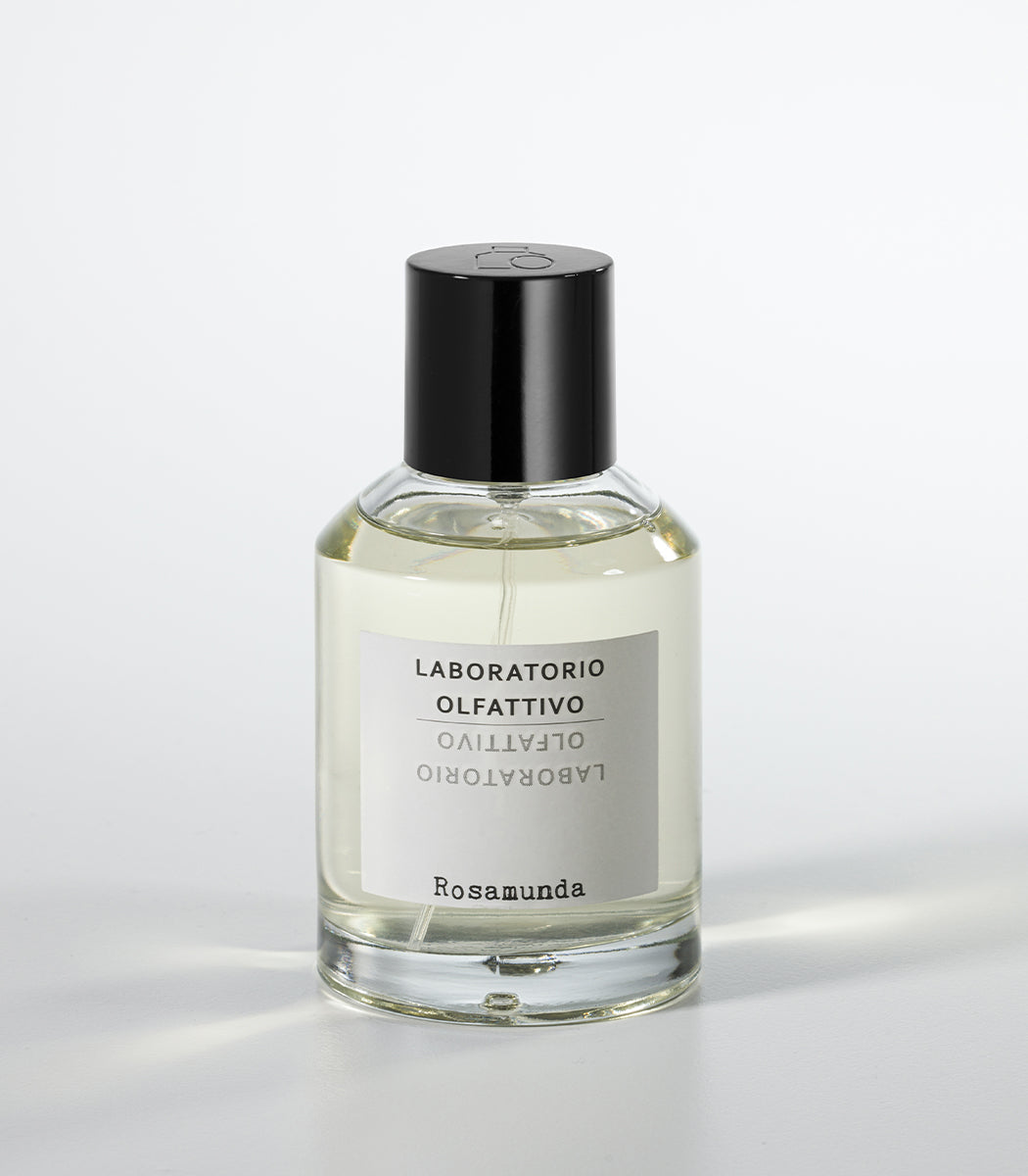 A clear glass perfume bottle with a black cap and a white label displays the brand Laboratorio Olfattivo and the product Rosamunda, embodying neoclassical elegance against a plain white background.