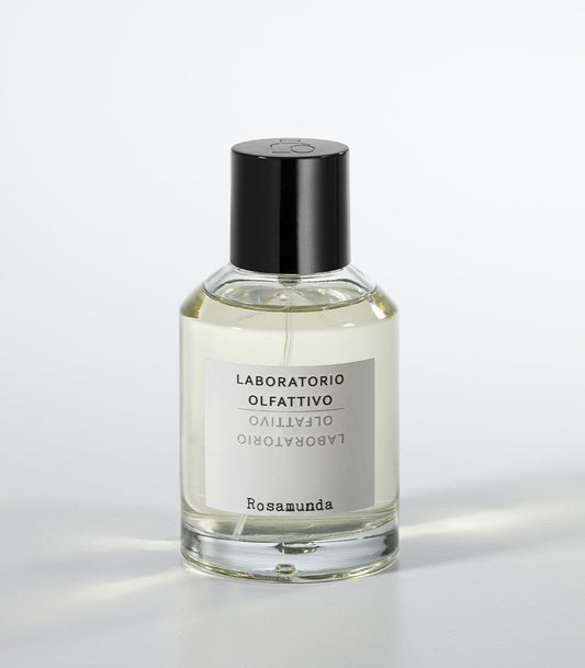 A clear glass perfume bottle with a black cap and a white label displays the brand Laboratorio Olfattivo and the product Rosamunda, embodying neoclassical elegance against a plain white background.