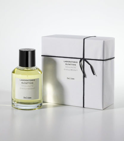 A bottle of Salina Eau de Parfum by Laboratorio Olfattivo stands beside a white gift box tied with black string, both labeled with the brand and fragrance name, on a plain light gray background.