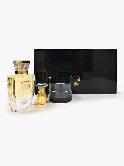 The Emarati Musk Trio Shield Edition Gift Box by Hind Al Oud is displayed on a white surface, featuring luxury perfume bottles, including Al Qasr Oud Muattar, and a black cylindrical container in front of a glossy black box with gold logo and Arabic text.