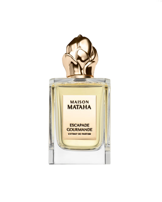 A glass bottle of Maison Mataha Escapade Gourmande Extrait de Parfum, featuring a rose-shaped gold cap and light yellow liquid, set against a white background—a vanilla scent with crème brûlée notes.