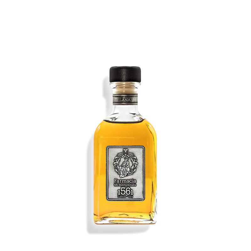 A clear glass bottle of golden Lana DIFFUSER by Farmacia SS. Annunziata 1561, adorned with a silver label and black cap, brings refined Arte della Lana scents to any room. Displayed against a white background.