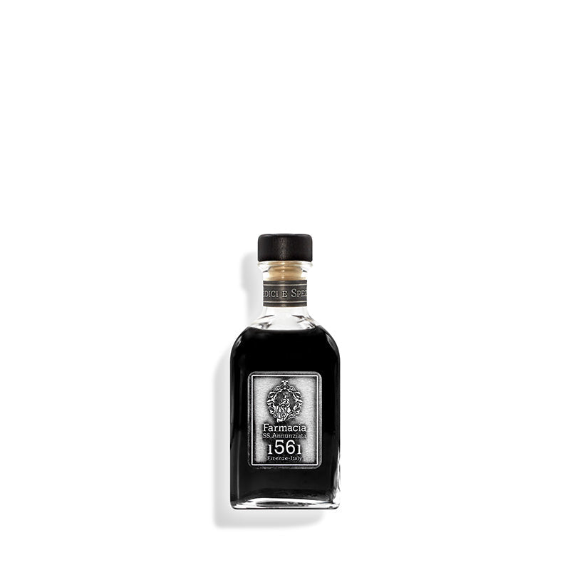 A small glass bottle of Farmacia SS. Annunziata 1561 Medici e Speziali DIFFUSER, with a black cap and vintage-style label, is centered on a white background. Black reeds suggest it diffuses a subtle, peppery scent into the air.