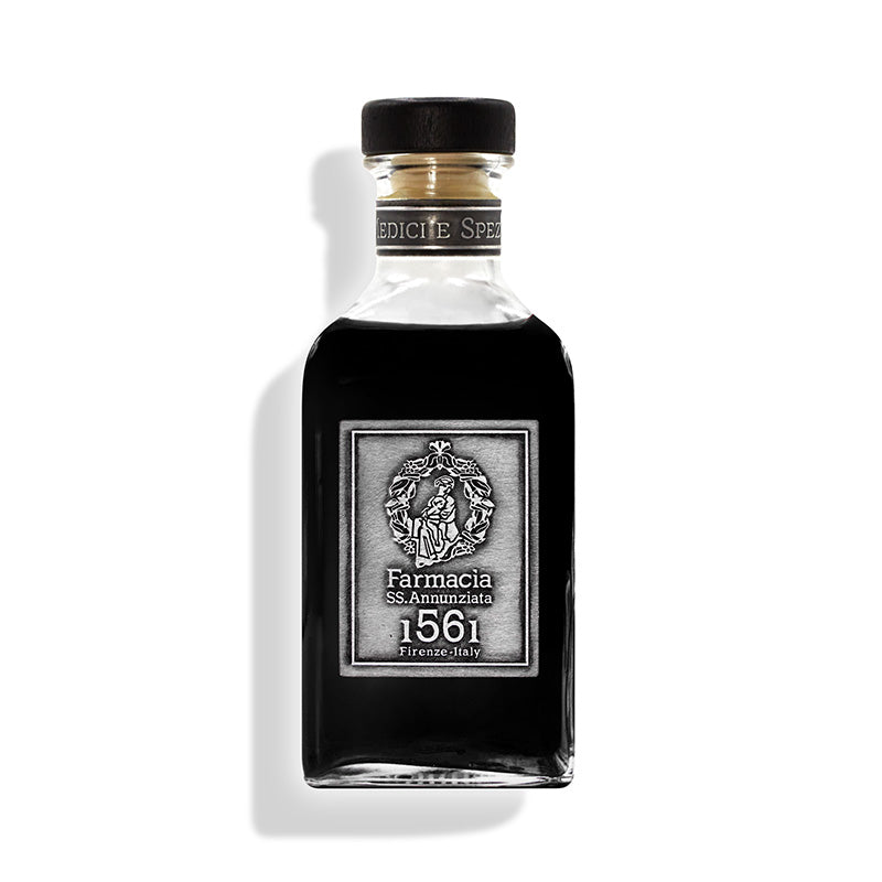 A clear glass Medici e Speziali DIFFUSER by Farmacia SS. Annunziata 1561 features dark liquid, a black cap, silver label, and black sticks emerging from the top, hinting at a peppery scent. It casts a shadow on the white background.