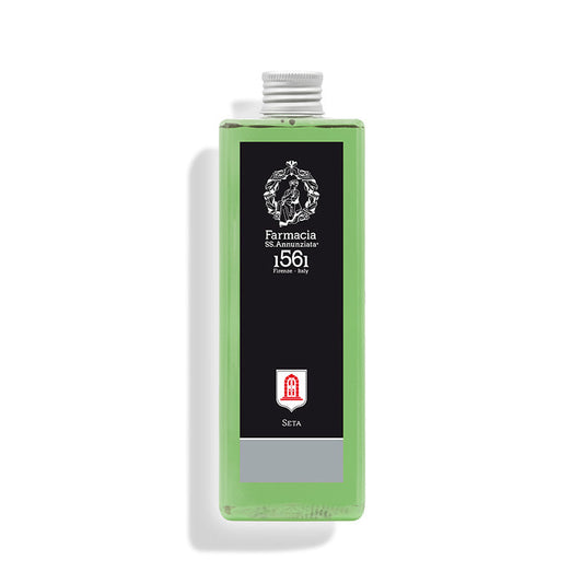 A rectangular bottle of green liquid with a silver cap and black label featuring “Farmacia SS. Annunziata 1561 Firenze Italy,” a red emblem, and “SETA.” Seta REFILL evokes the refined Arte della Seta fragrance collection.