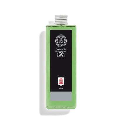 A rectangular clear bottle holds Seta REFILL – Farmacia home fragrance by Farmacia SS. Annunziata 1561, featuring light green liquid, a black label with white text and red symbol, and a silver cap—an elegant diffuser refill.