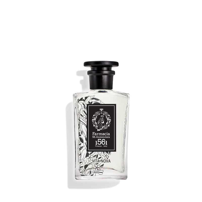 A clear glass Vita Nova Eau de Parfum by Farmacia SS. Annunziata 1561 features a black cap and black-and-white floral design; hints of pink pepper intrigue as the bottle casts a soft shadow on a white background.