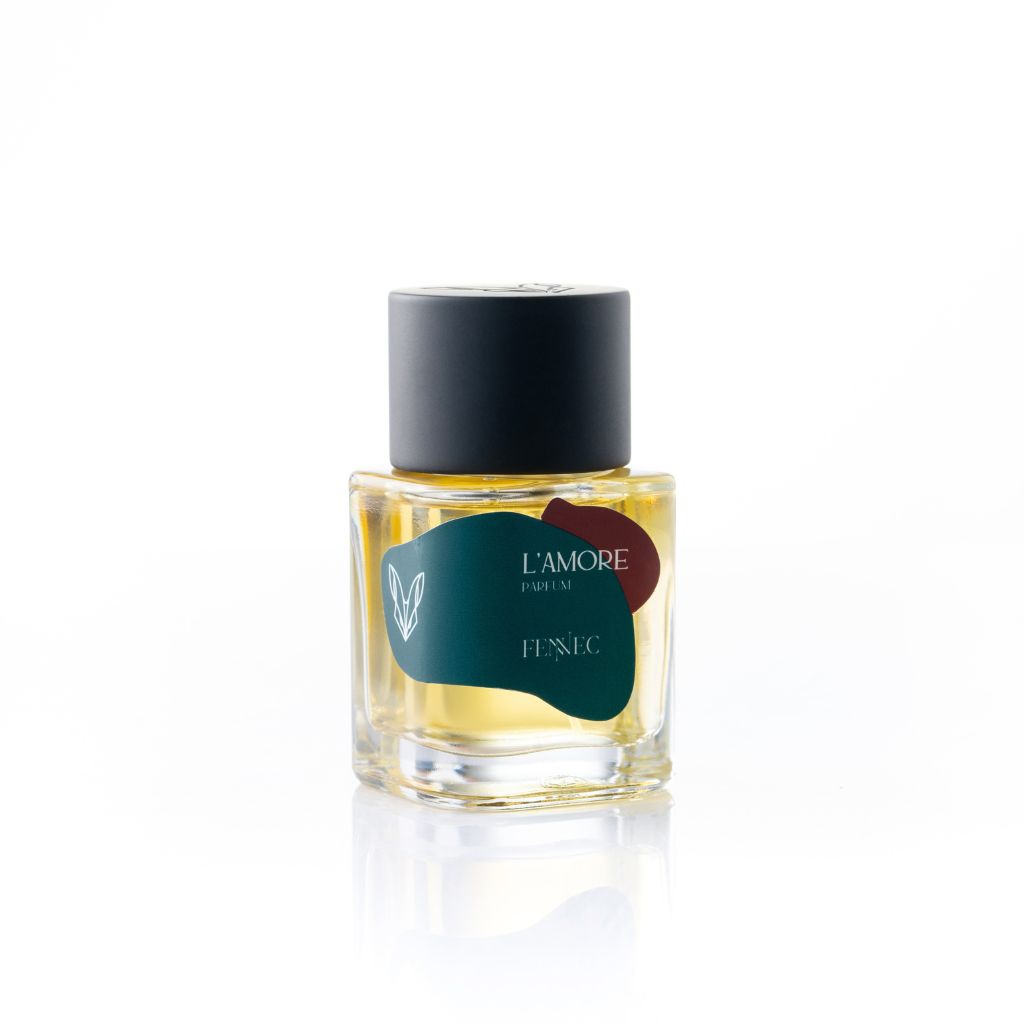 A glass bottle of L'Amour EDP by Fennec, featuring a dark green and burgundy design inspired by the North African desert and a black cylindrical cap, is set against a white background.