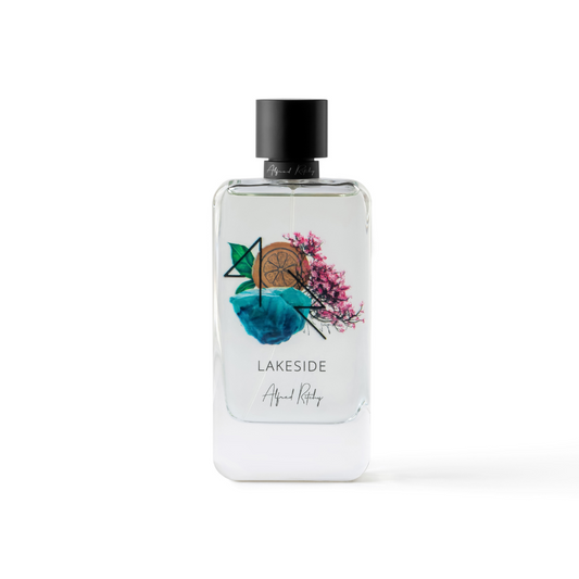 A 100ml clear LAKESIDE Eau de Parfum by Alfred Ritchy, with a black cap and blue watercolor label featuring a lime slice, green leaves, and pink flowers—adds a refreshing touch to the LAKESIDE collection.