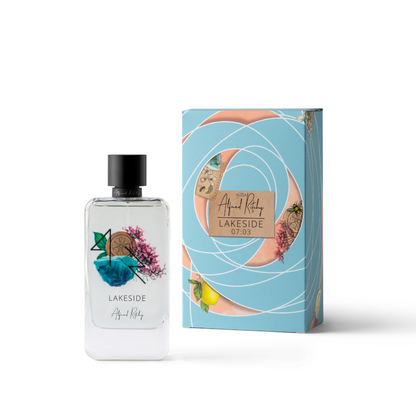 A clear 100ml LAKESIDE Eau de Parfum bottle by Alfred Ritchy stands beside its blue, floral-patterned box with green leaves and citrus slices, reflecting the Blossomfall fragrance.