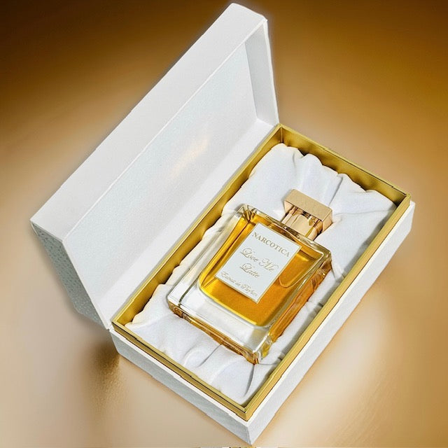 A bottle of Love Me Latte Eau de Parfum by Narcotica rests in a white and gold box lined with white fabric, set against a gold gradient background—an extrait de parfum promising an unforgettable scent experience.