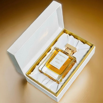 A bottle of Love Me Latte Eau de Parfum by Narcotica rests in a white and gold box lined with white fabric, set against a gold gradient background—an extrait de parfum promising an unforgettable scent experience.