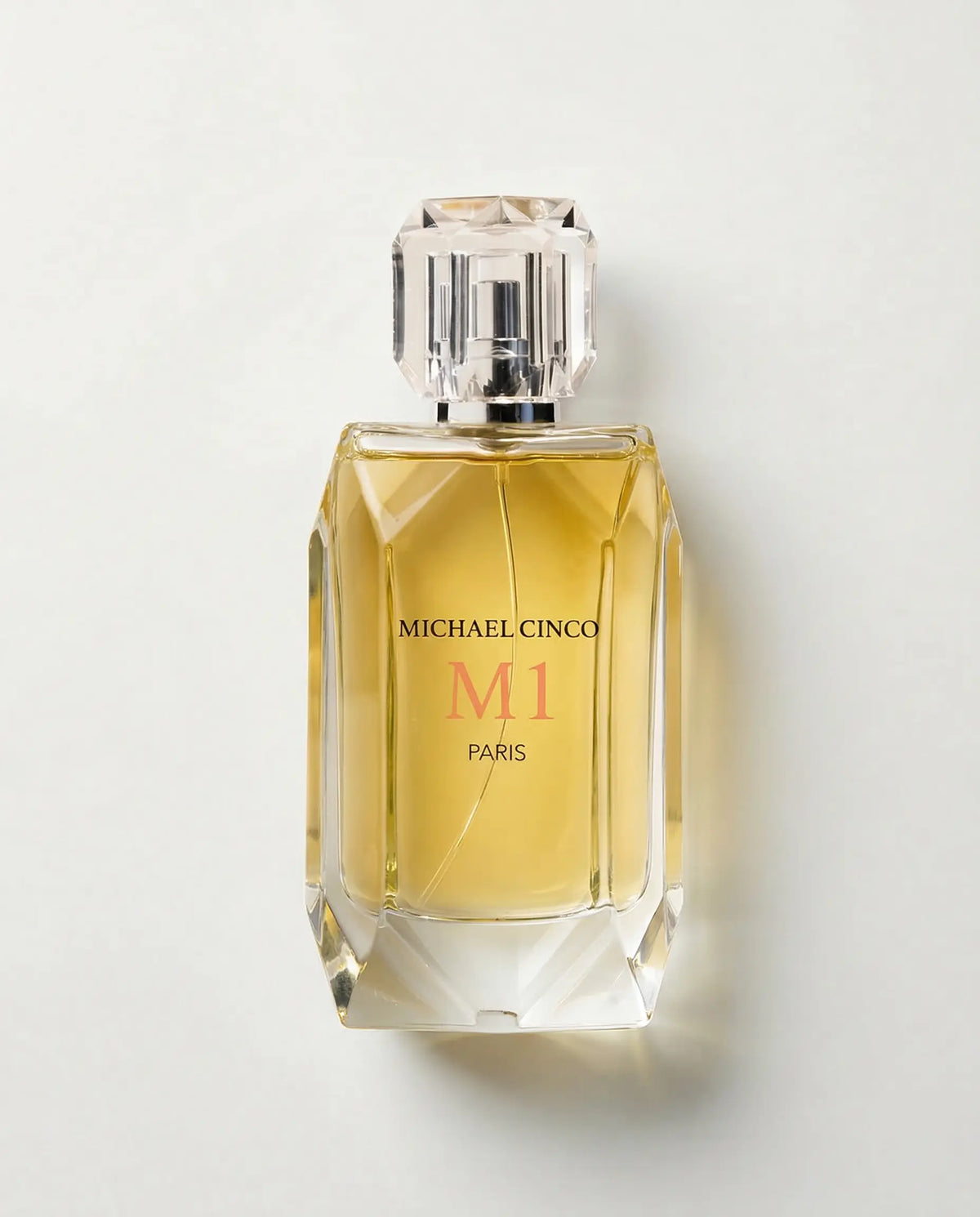 Michael Cinco M1 Paris perfume bottle with a faceted clear glass design, filled with golden-yellow liquid, on a light gray background.