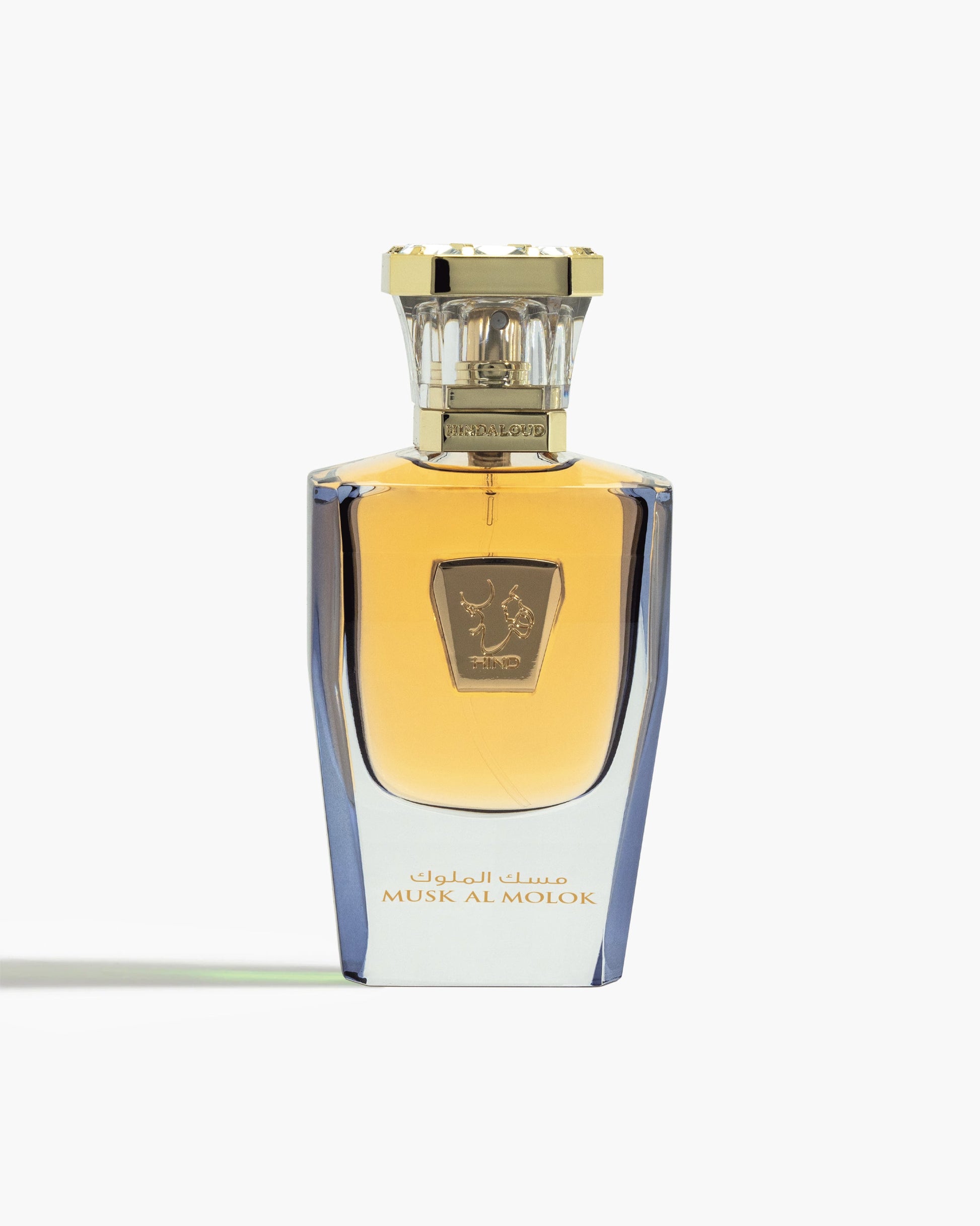 A luxurious glass bottle with gold accents and Arabic script, labeled Musk Al Molok Parfum by Hind Al Oud, filled with amber-hued floral musk fragrance, stands upright against a white background.