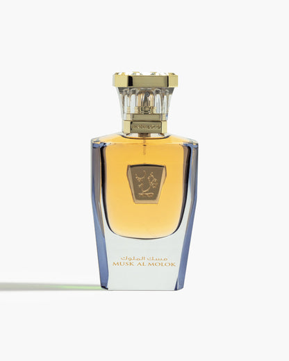 A luxurious glass bottle with gold accents and Arabic script, labeled Musk Al Molok Parfum by Hind Al Oud, filled with amber-hued floral musk fragrance, stands upright against a white background.