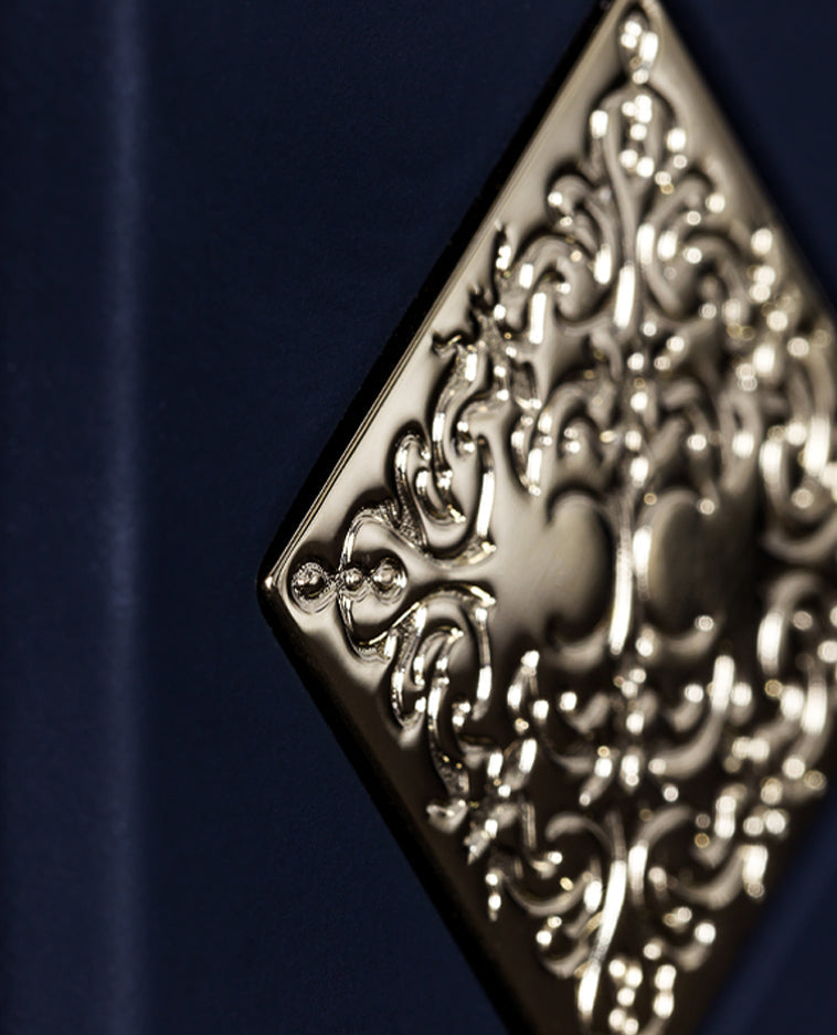 Close-up of an ornate, gold embossed pattern on a diamond-shaped plaque set against dark blue, evoking the luxurious essence of INITIO’s Magnetic Blend 1 Eau de Parfum and its signature ambergris allure.