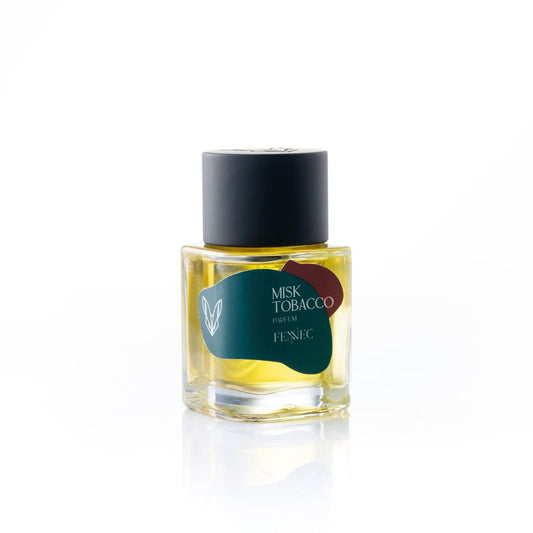 A clear glass perfume bottle with yellow liquid, labeled Misk Tobacco Parfum by Fennec, has a black cap and a green and red abstract label inspired by North African desert colors, displayed against a white background.
