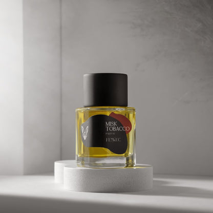 A glass Fennec Misk Tobacco Parfum bottle with a black cap rests on a round white pedestal in soft, minimalist light. The yellow liquid hints at fragrance notes inspired by the North African desert.