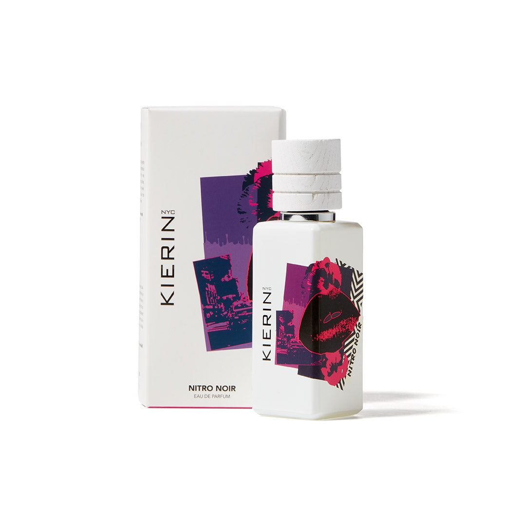 A white bottle of Kierin Nitro Noir Eau de Parfum is displayed in front of its box, both featuring bold abstract purple and red designs with cityscape and lips—an eye-catching choice for any luxury fragrance collection.