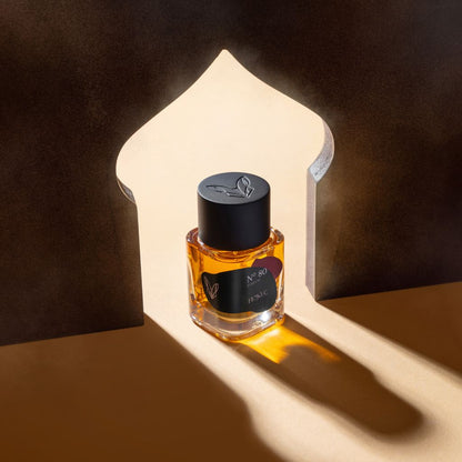 A bottle of Fennec N80 Parfum, with amber liquid, rests in a beam of light within an arched cutout casting dramatic shadows on beige. The black-capped bottle has a black label with gold details, evoking the allure of North Africa’s desert fox.