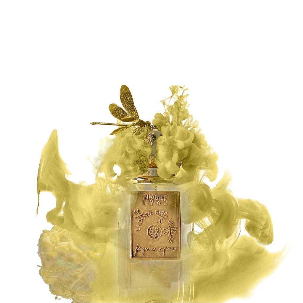 The LA DANZA DELLE LIBELLULE EDP by Nobile 1942 features a perfume bottle with a gold plaque and gold dragonfly on the cap, surrounded by swirling yellow mist on a white background.