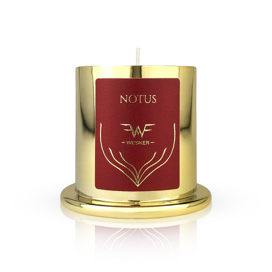 The Notus Candle - Wesker by Wesker is a gold metallic candle with a red label featuring gold designs and "WESKER" below "NOTUS." Infused with a desert scent, it sits on a matching gold base against a white background.