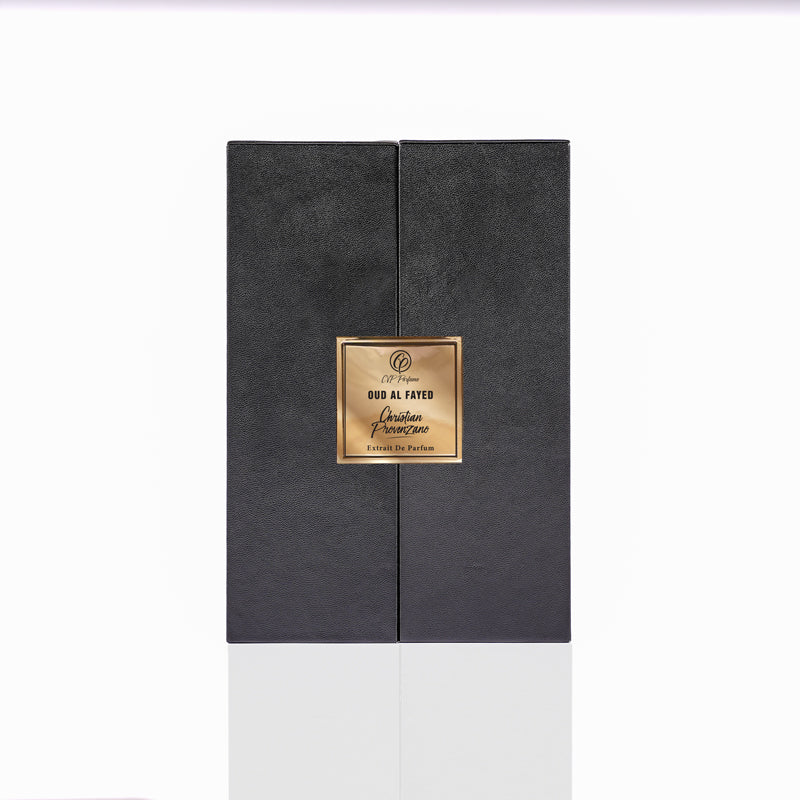 A black rectangular perfume box with a gold label displaying "Oud al Fayed Eau de Parfum - Christian Provenzano" exudes an exotic woody, oriental scent, elegantly showcased on a reflective white surface.