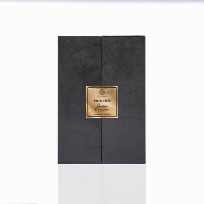 A black rectangular perfume box with a gold label displaying "Oud al Fayed Eau de Parfum - Christian Provenzano" exudes an exotic woody, oriental scent, elegantly showcased on a reflective white surface.