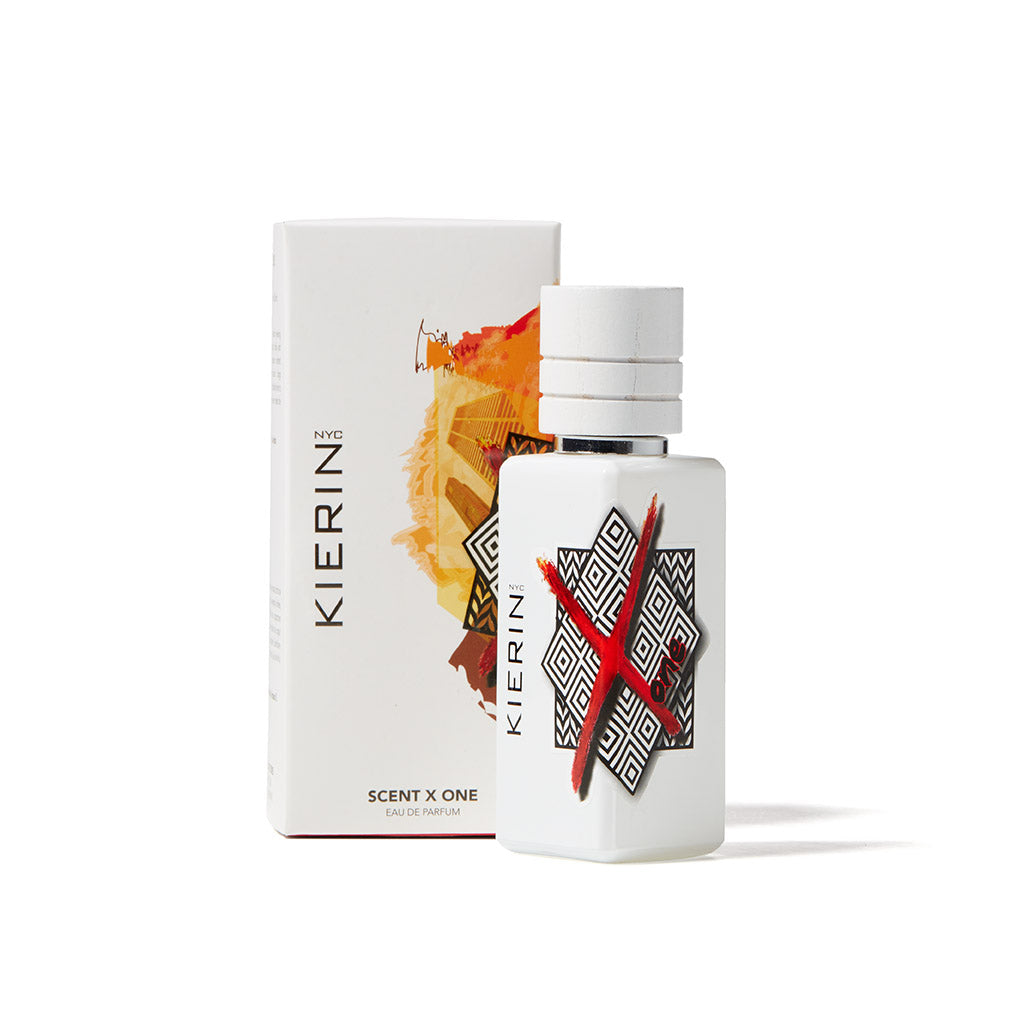 A white bottle of ScentXOne Eau de Parfum by Kierin, featuring bold black and red geometric designs, stands before its box adorned with abstract orange-red art—a premium niche fragrance by Kierin with long-lasting luxury scent appeal.