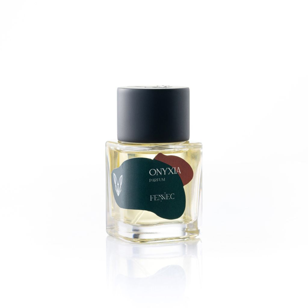 A small glass perfume bottle with a black cap and a green-burgundy label displays "Onyxia Parfum" by Fennec, plus a white fennec fox head logo—honoring this North African animal’s large ears.