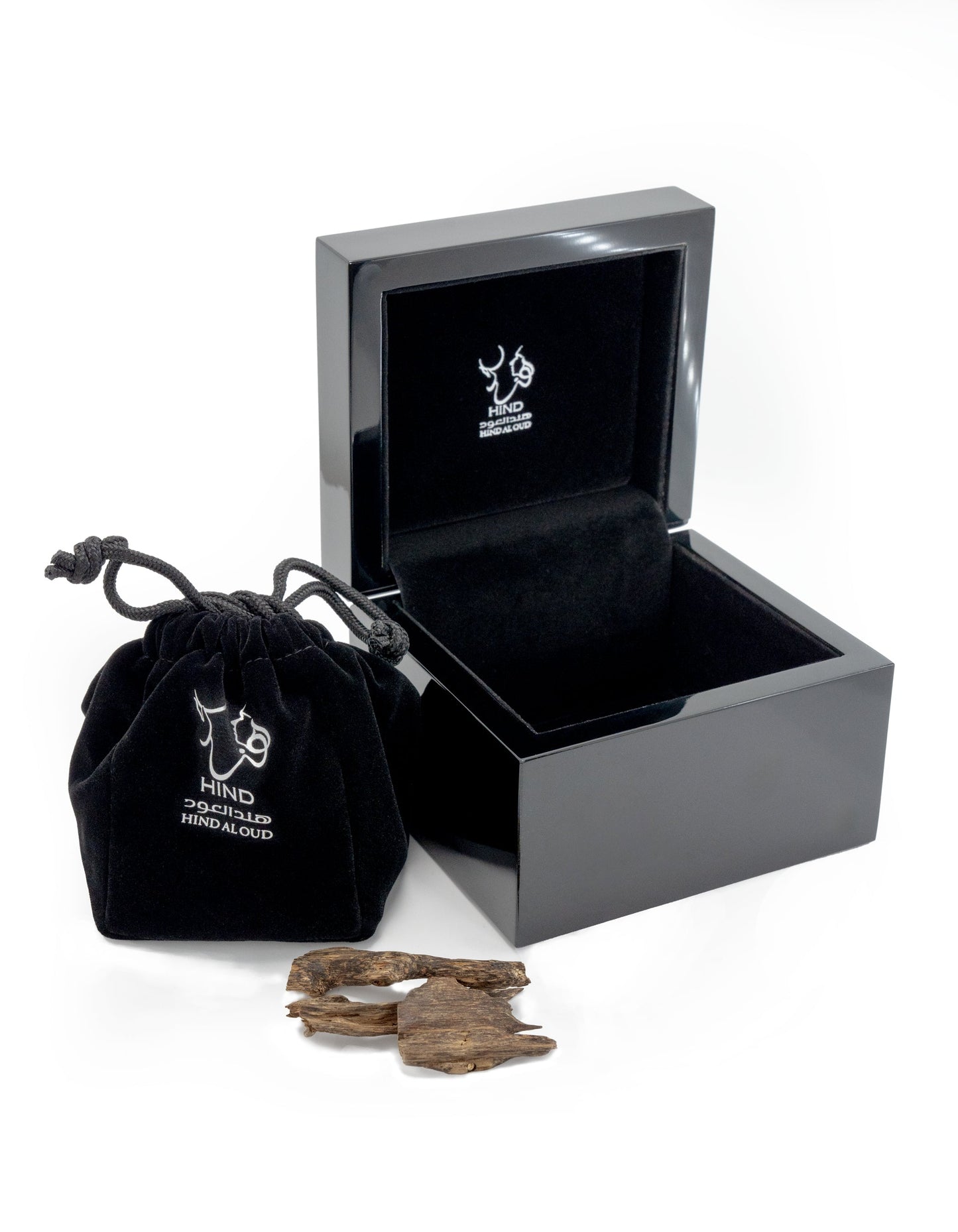 A glossy black jewelry box and a matching drawstring pouch, both with white Hind Al Oud logos, sit beside pieces of textured Oud Amiri Natural Oud, capturing the signature luxury of Hind Al Oud.