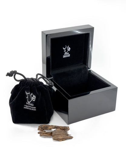 A glossy black jewelry box and a matching drawstring pouch, both with white Hind Al Oud logos, sit beside pieces of textured Oud Amiri Natural Oud, capturing the signature luxury of Hind Al Oud.