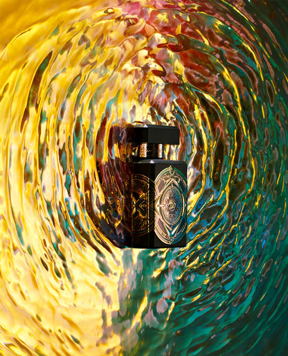A black and gold INITIO Oud For Happiness Eau de Parfum bottle stands amid vibrant yellow, green, and pink swirls, capturing the luxurious allure of this woody spicy fragrance.