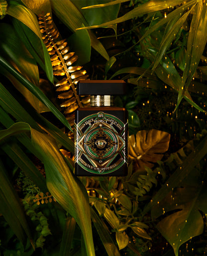 The Oud For Happiness Eau de Parfum by INITIO features a decorative black bottle with gold and green accents, set among lush leaves and golden ferns, evoking its woody spicy scent in a luxurious, jungle-inspired setting.