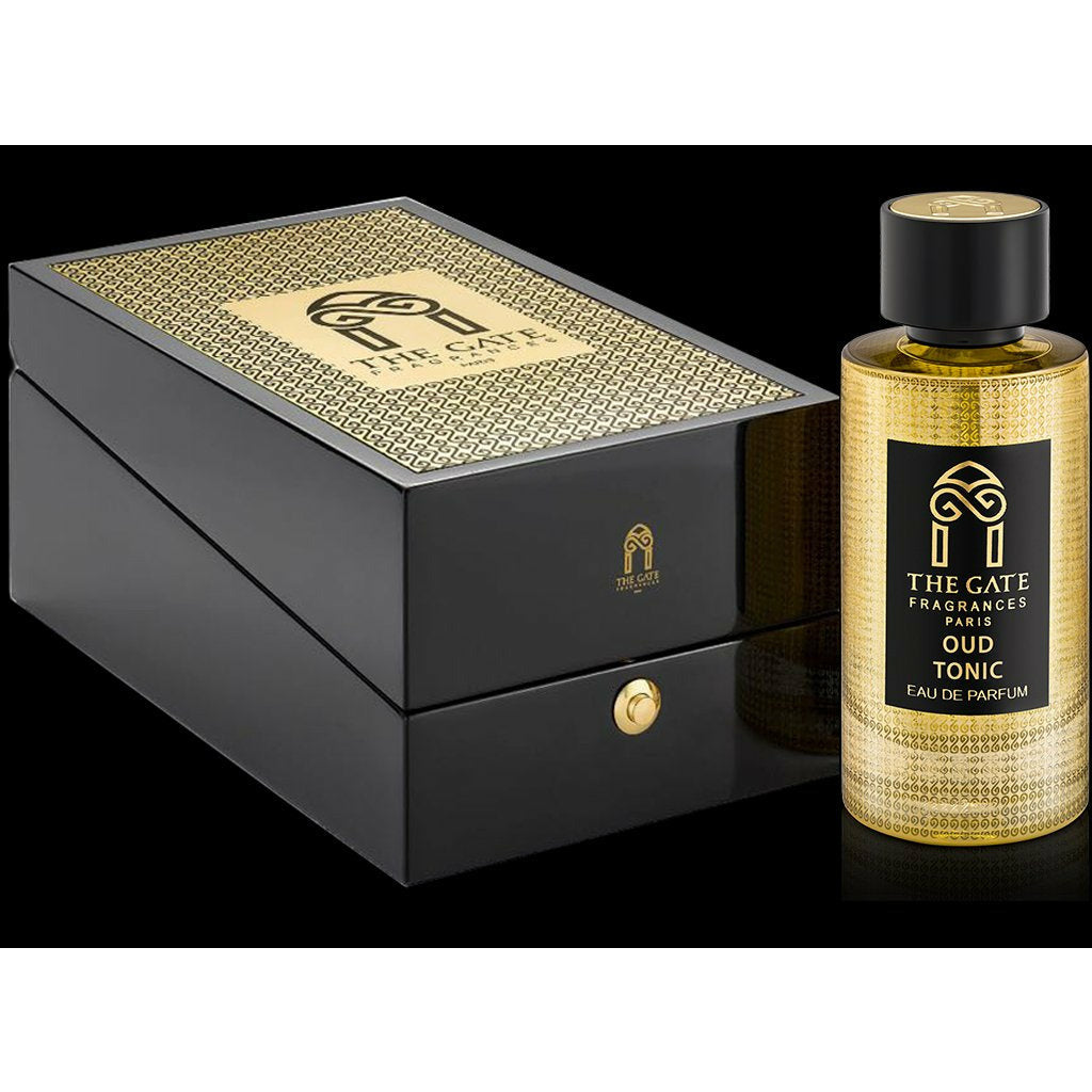 A gold and black bottle of Oud Tonic Eau de Parfum by The Gate Paris stands beside a matching textured box showcasing the brand’s logo and name.